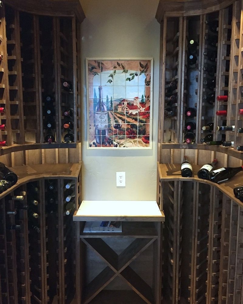 Cozy wine cellar featuring wooden racks, a small table, and a vineyard-themed artwork on the wall.