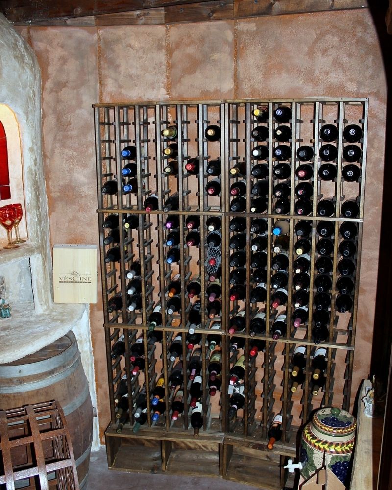 A wooden wine rack filled with various bottles of wine in a rustic cellar setting.