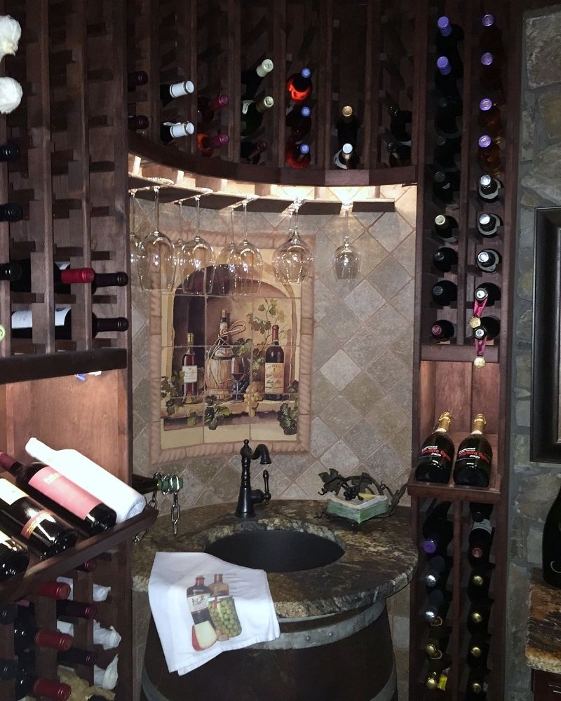 Wine cellar featuring wooden racks for bottles, a granite countertop, and glassware hanging above. Cozy and elegant atmosphere.
