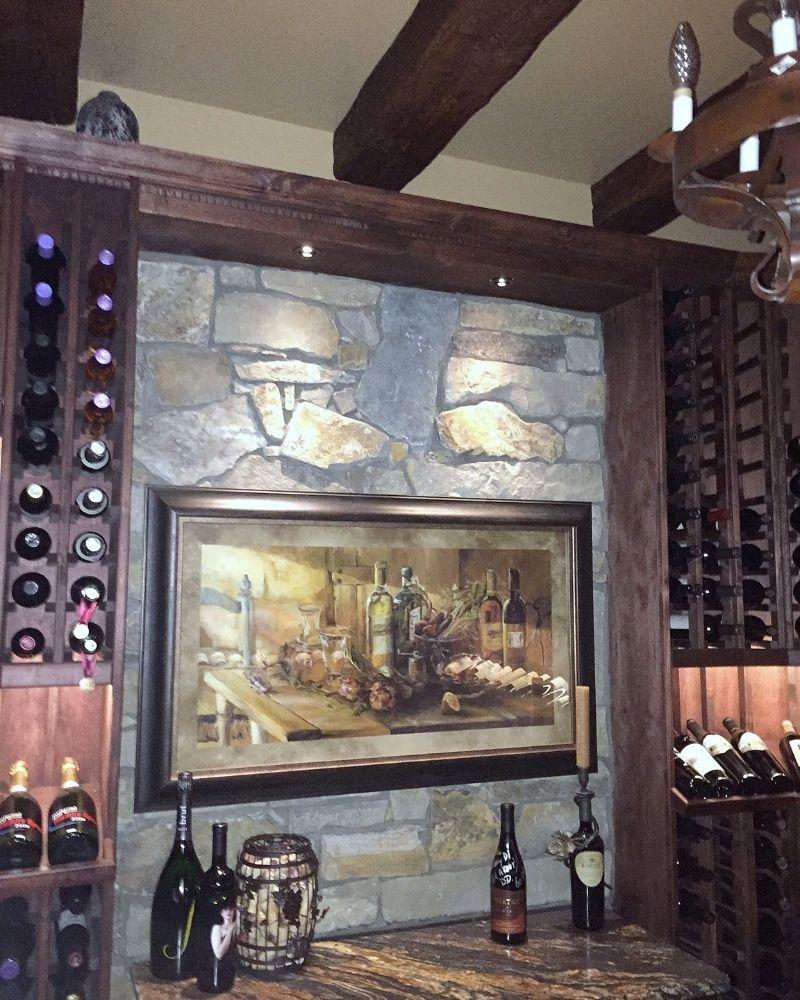 Elegant wine cellar featuring art, stone walls, and a variety of wine bottles displayed on wooden racks.