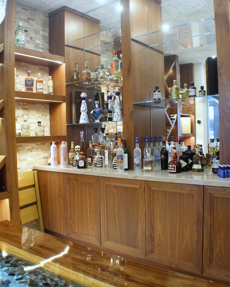 Stylish bar showcasing a variety of liquor bottles on wooden shelves, illuminated in a modern setting.