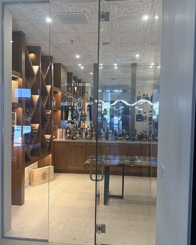 Elegant glass door entrance to a stylish home bar with a wooden shelf, displaying various bottles and a modern design.