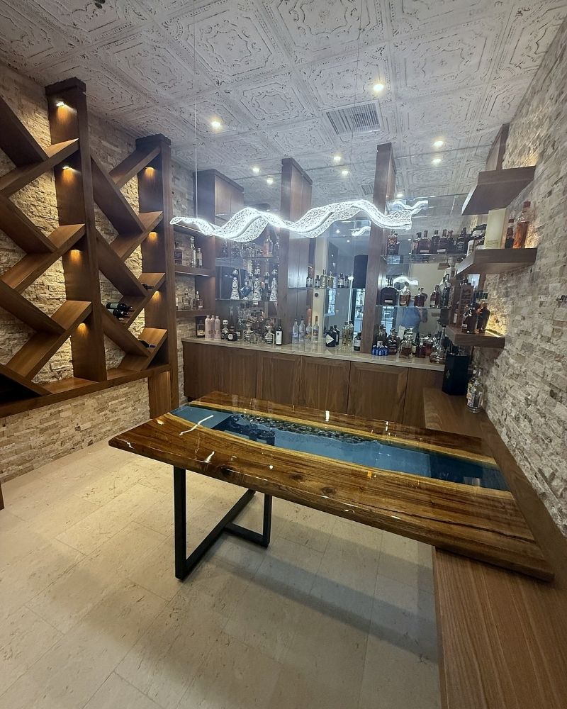 Stylish home bar with a wooden table, illuminated decor, and a variety of bottles on display in a modern interior.