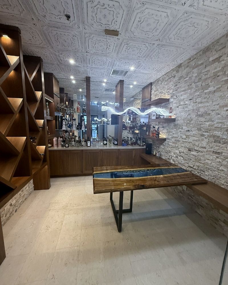 Modern bar interior with stylish wooden furniture, illuminated shelves, and a unique resin river table design.