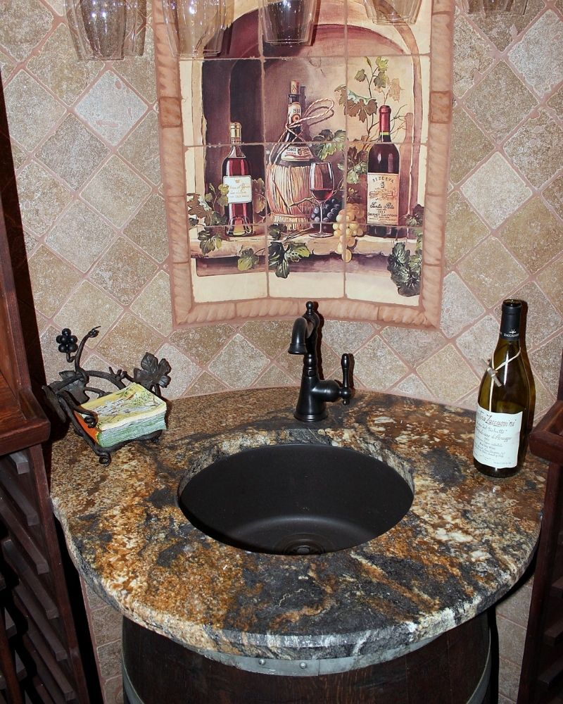 Elegant sink with black faucet on a granite counter, featuring a wine-themed wall art and decorative elements.