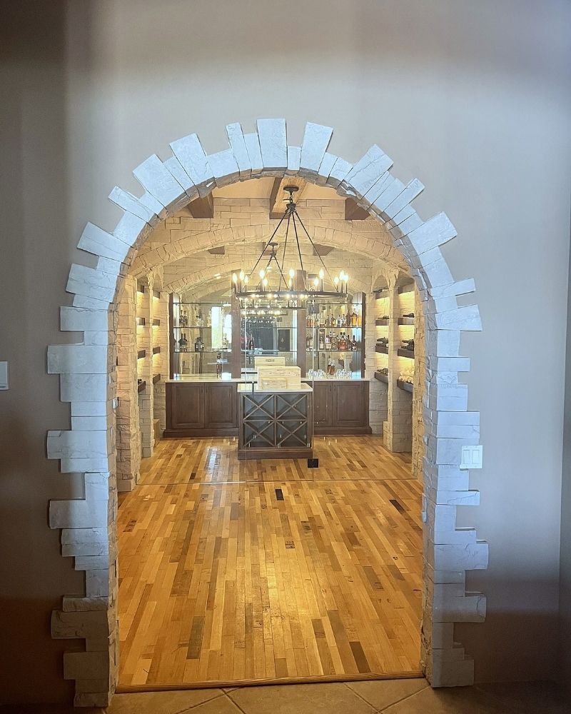 Stone archway leading to a stylish bar area with hardwood floors and elegant lighting. Perfect for entertaining guests.