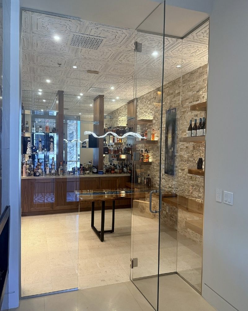 Stylish glass-entry bar area featuring a modern design, illuminated shelves, and a variety of spirits displayed.