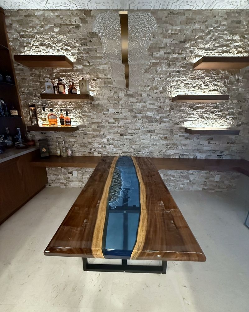 Completed Wine Cellar (58) Luxurious wooden table with epoxy resin, set against a textured stone wall and modern shelving, showcasing elegance.