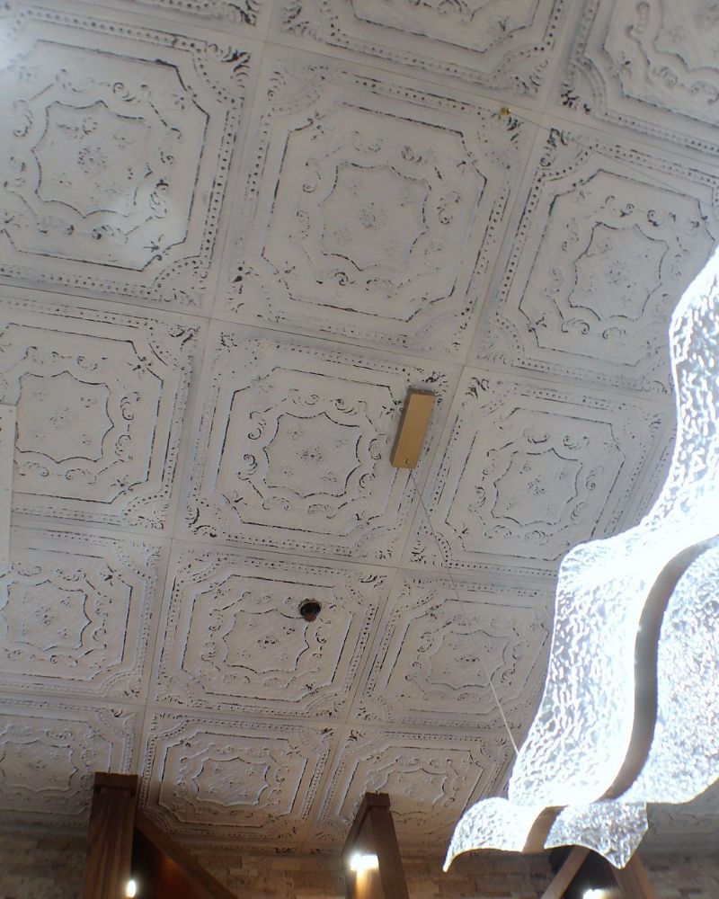 Ornate white vintage ceiling tiles with decorative patterns and modern lighting fixtures in a stylish interior space.