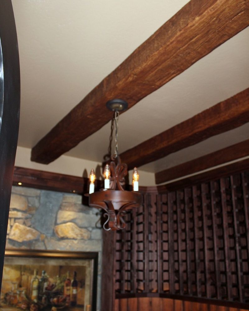 Rustic chandelier hanging from wooden beams in a cozy dining area, featuring stone walls and elegant decor.
