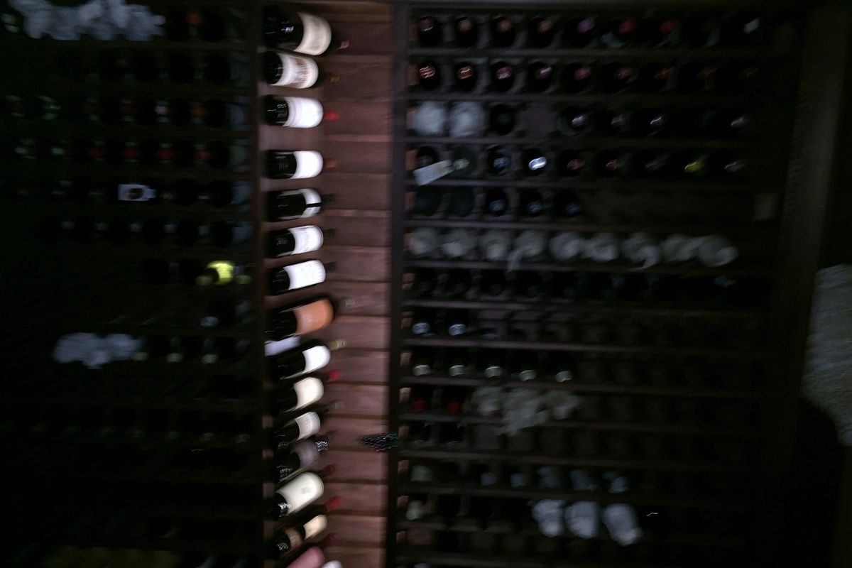 Dark wine cellar showcasing a wooden rack filled with various wine bottles, highlighting a well-stocked collection.