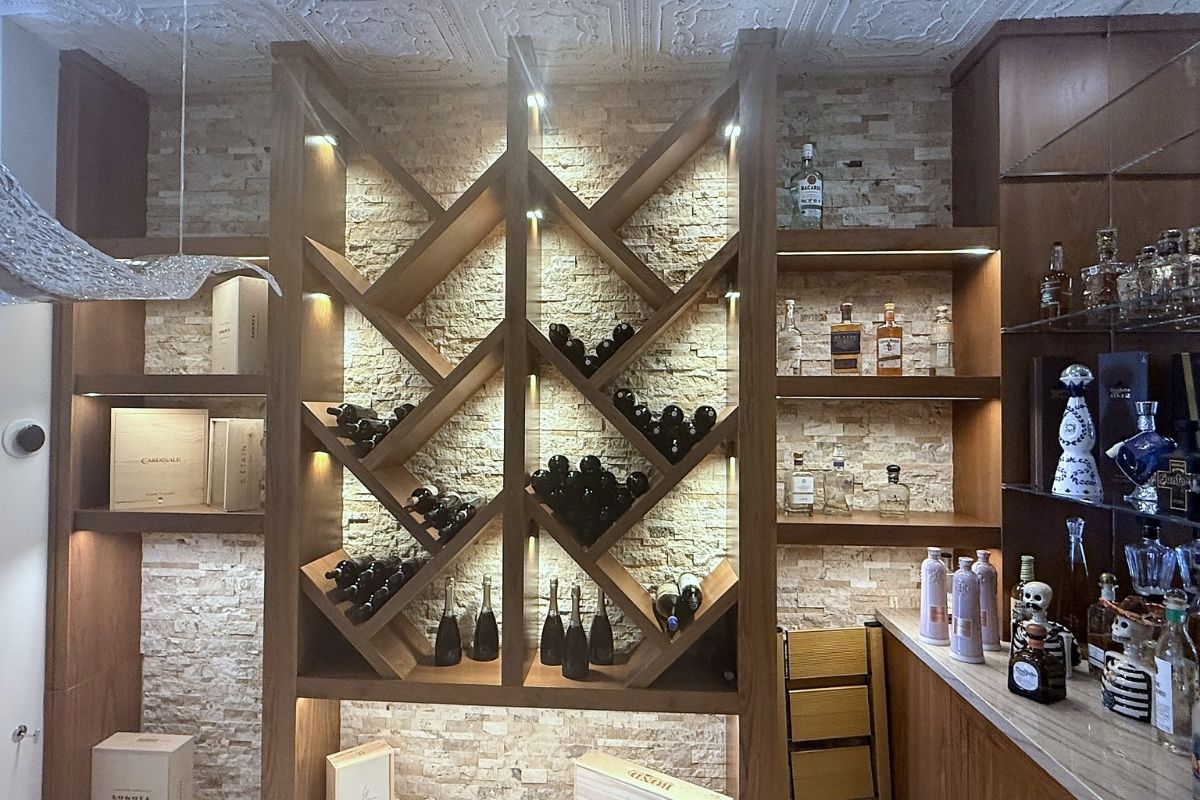 Elegant wine rack display with illuminated shelves showcasing various bottles against a textured stone wall backdrop.