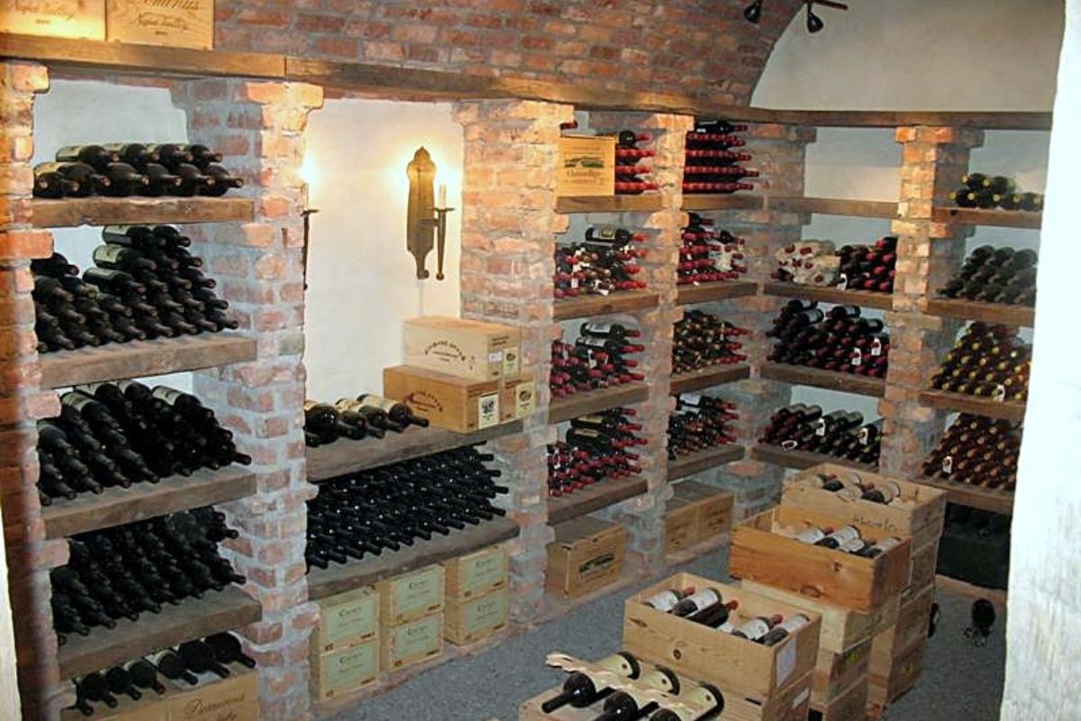 Well-organized wine cellar with wooden shelves filled with bottles and crates, featuring a rustic brick interior.