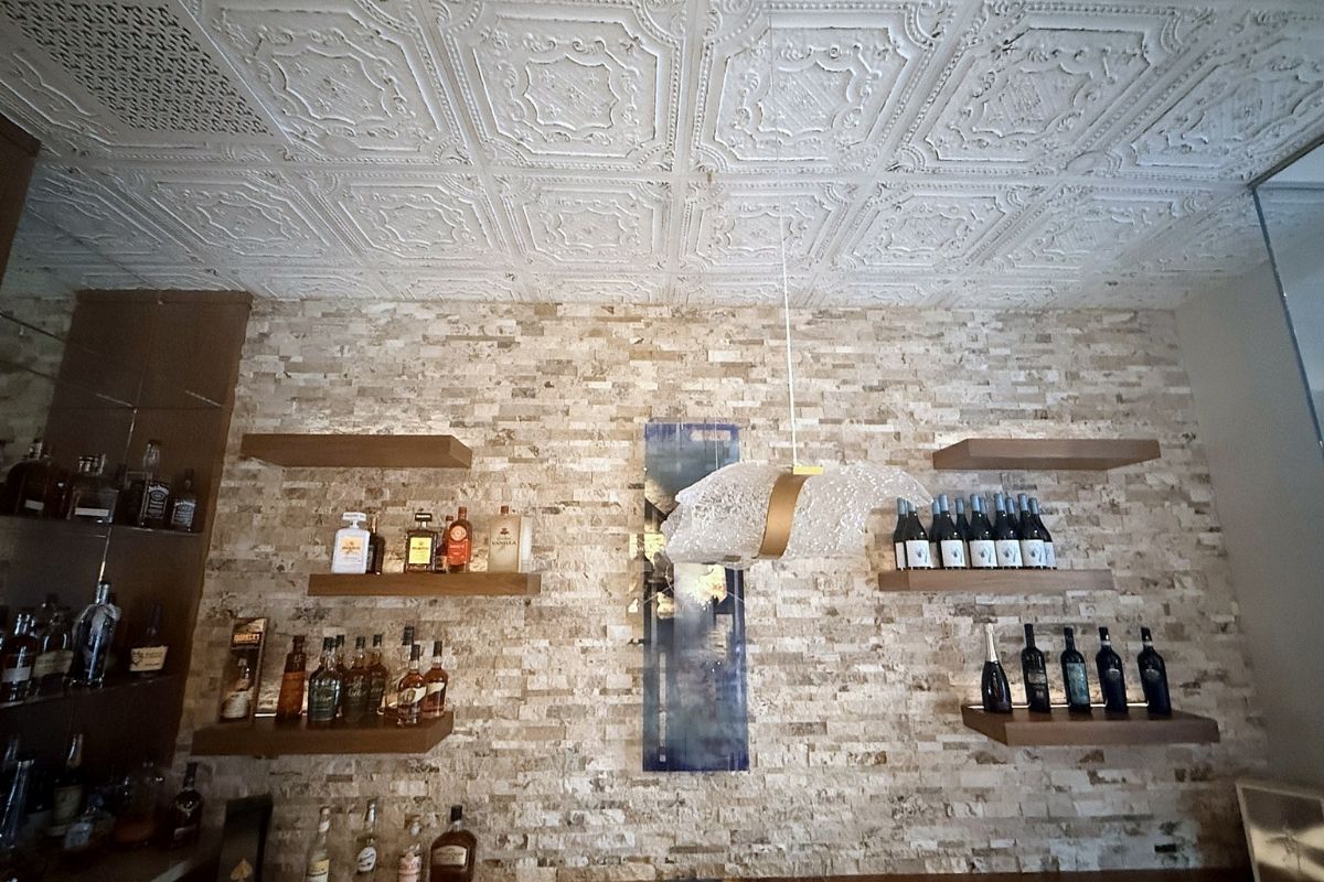 Stylish bar interior with textured ceiling, illuminated shelves displaying a variety of spirits and decorative wall art.