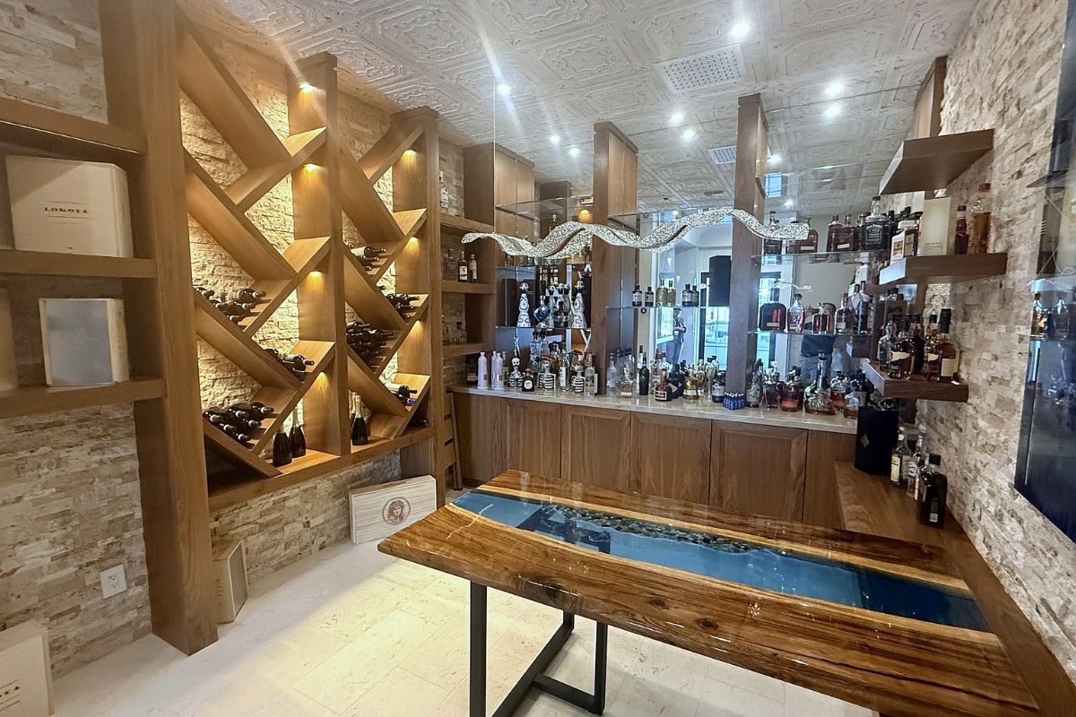 Stylish home bar featuring wine racks, a diverse liquor display, and a unique wooden table with resin inlay.
