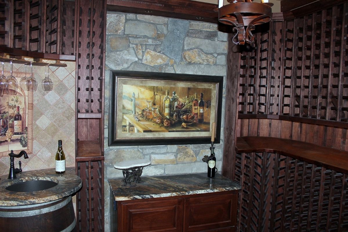 Rustic wine cellar featuring stone walls, wooden shelves, and vintage-inspired artwork with wine bottles displayed.