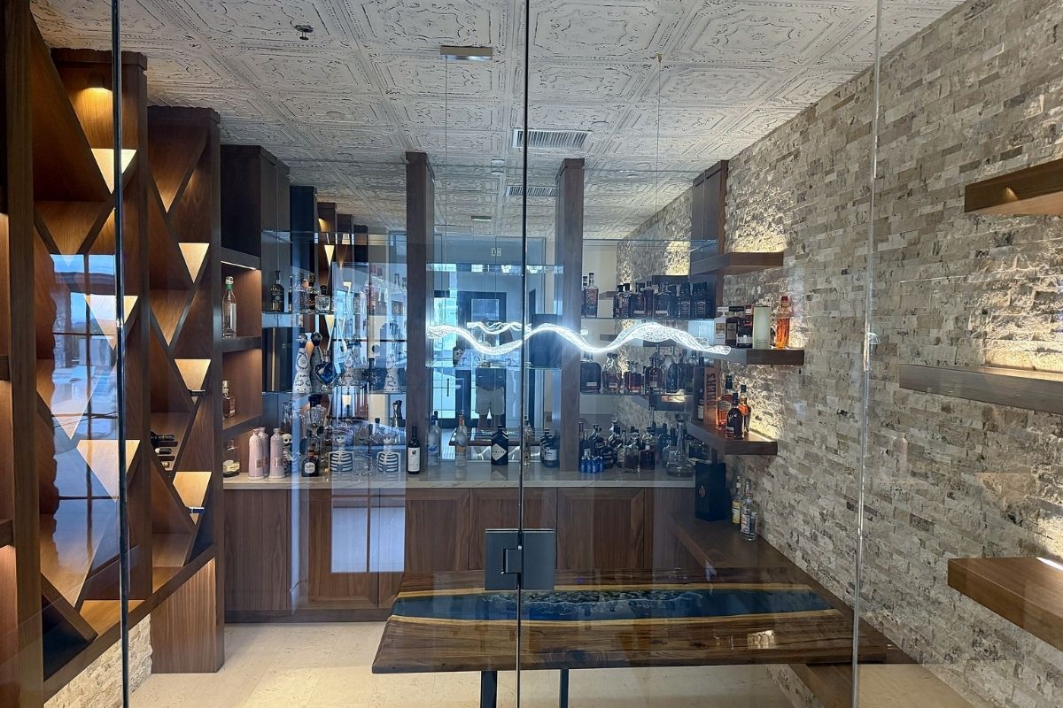 Modern home bar with wooden shelves displaying a variety of spirits, glass walls, and stylish decor.