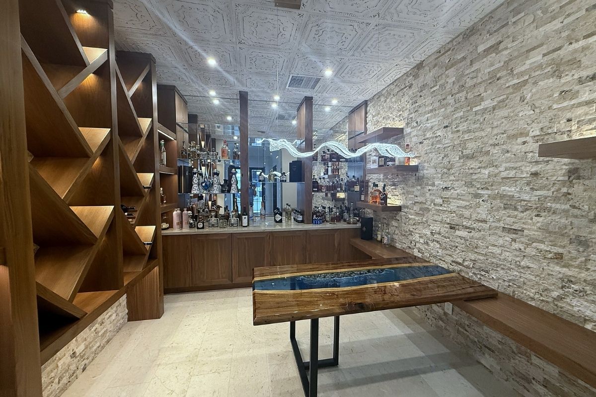 Stylish modern bar area featuring a unique wooden table, stone walls, and an array of liquor bottles on display.
