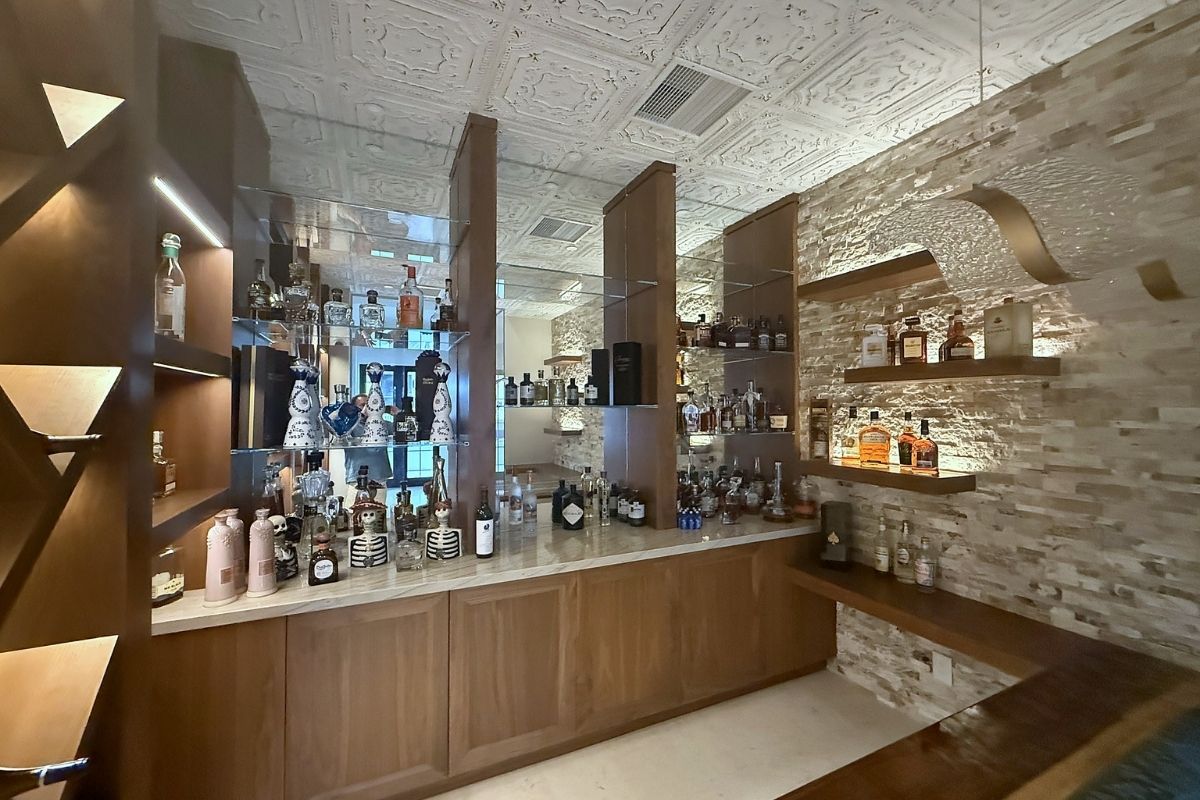 Elegant home bar featuring a variety of spirits displayed on wooden shelves and illuminated glass, with textured stone walls.