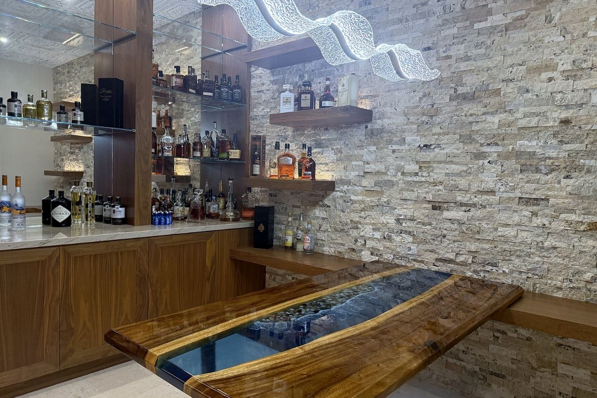 Luxurious home bar with wooden shelves, various spirits, and an elegant table featuring a resin-filled design.