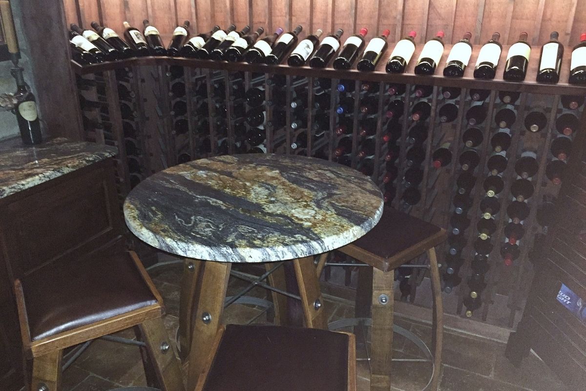 Cozy wine cellar featuring a round granite table, wooden stools, and a wall of carefully arranged wine bottles.