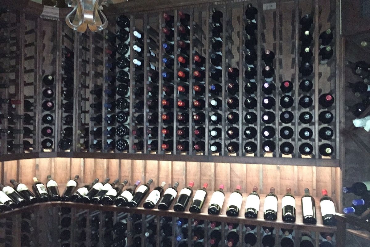 Wooden wine rack filled with various wine bottles, displaying an organized collection in a dimly lit cellar.