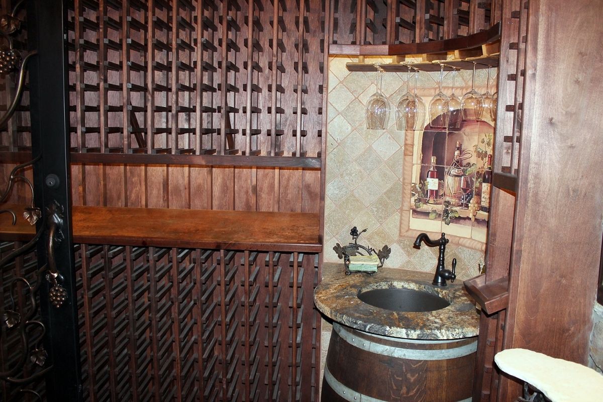 Elegant wine cellar design featuring wooden shelves, a barrel sink, and decorative glassware hanging above.