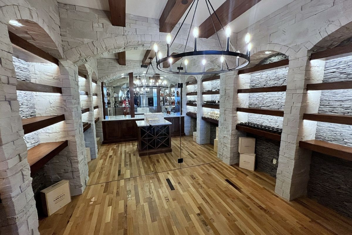 Stylish wine cellar with stone walls, wooden shelves, and a modern chandelier, perfect for wine enthusiasts.