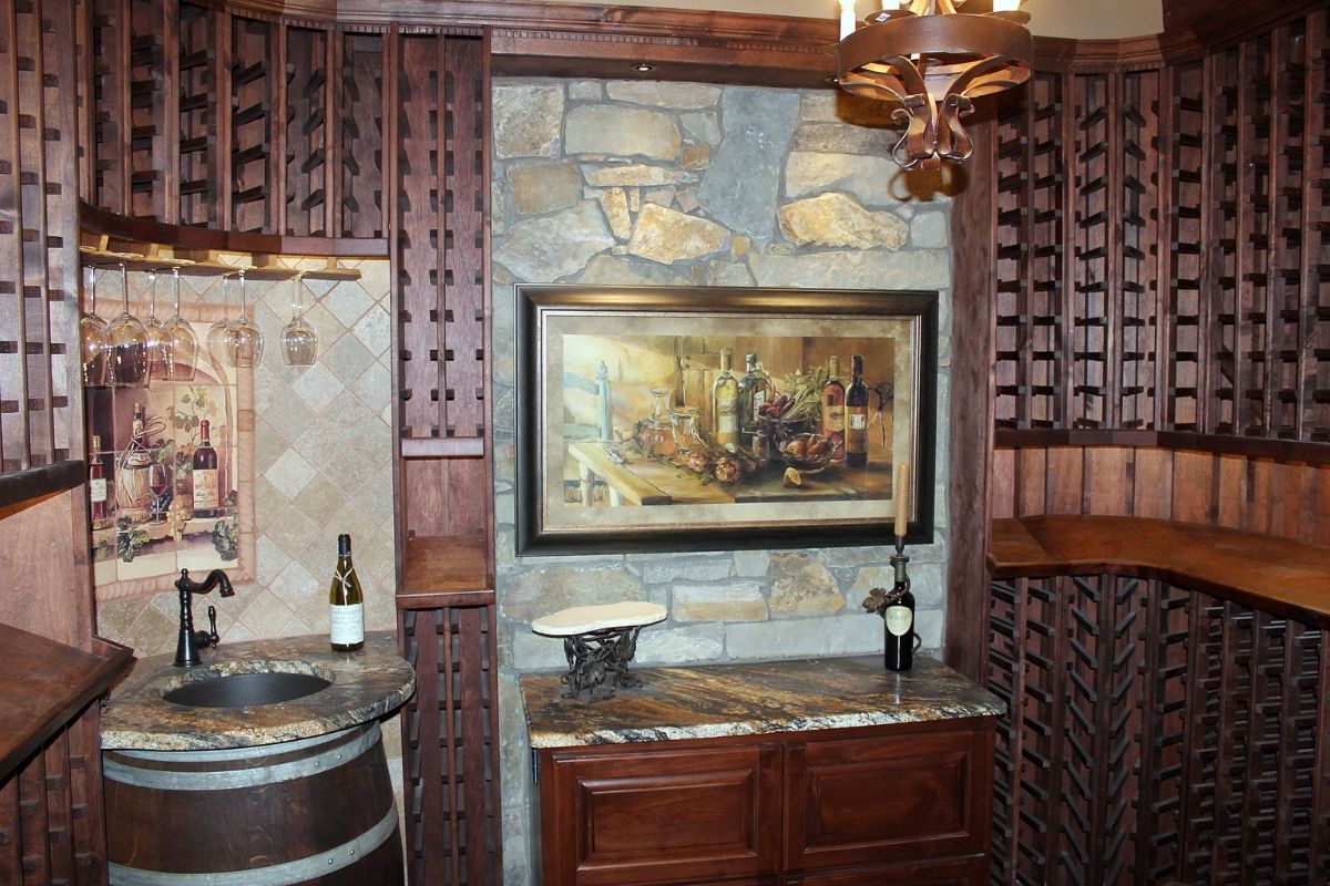 Elegant wine cellar featuring wooden racks, stone walls, artwork, and a granite countertop with wine accessories.