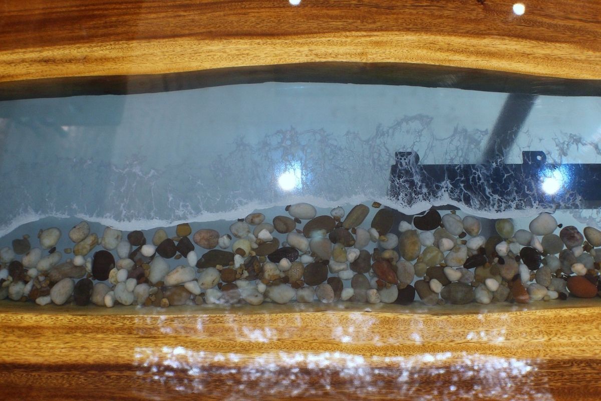 Wooden table with resin river layer revealing smooth pebbles and water-like ripples for a stunning nature-inspired design.
