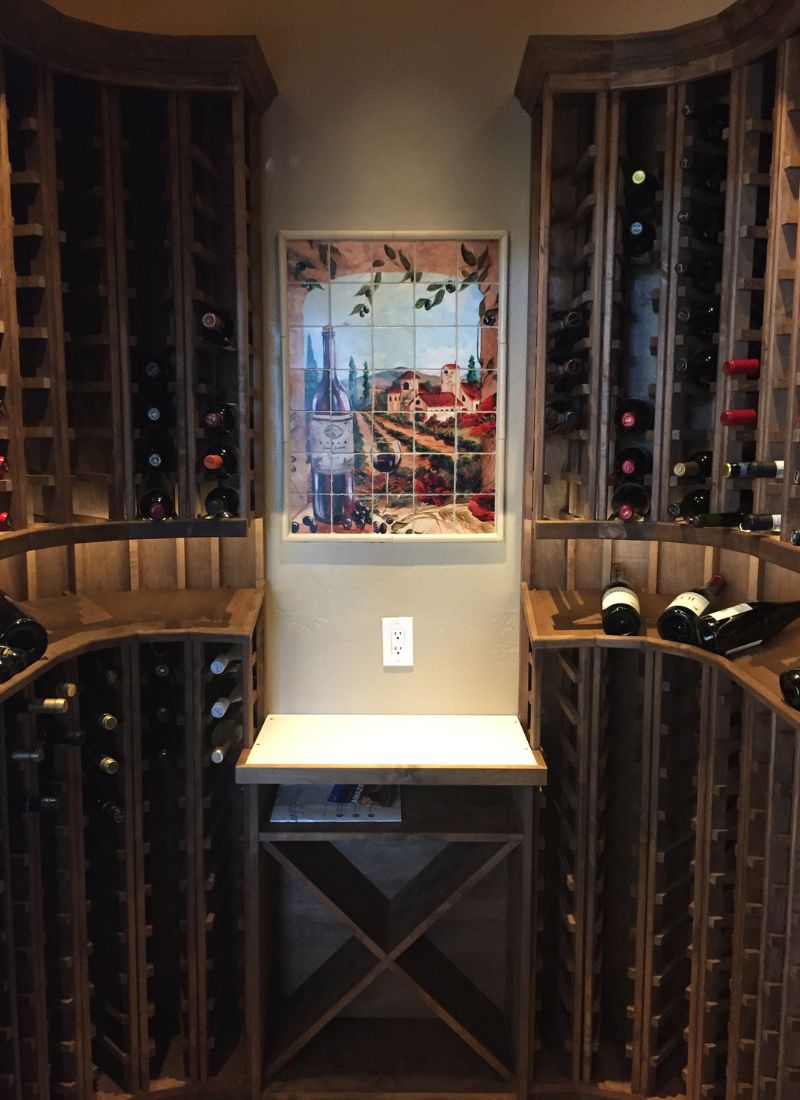 Alt text: Elegant wine cellar featuring wooden racks, a countertop, and a colorful wine-themed tile artwork.