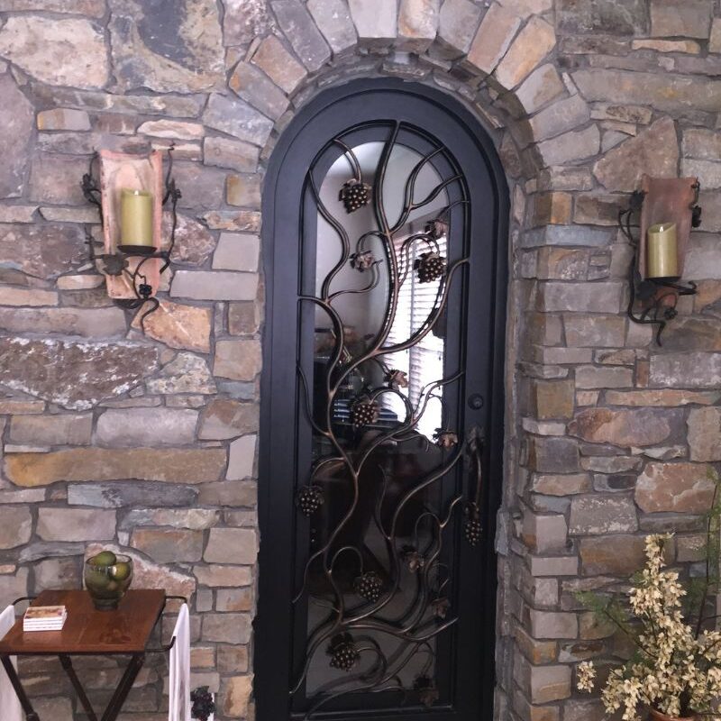 Elegant arched door with decorative metalwork on a stone wall, accented by candle sconces and natural decor.