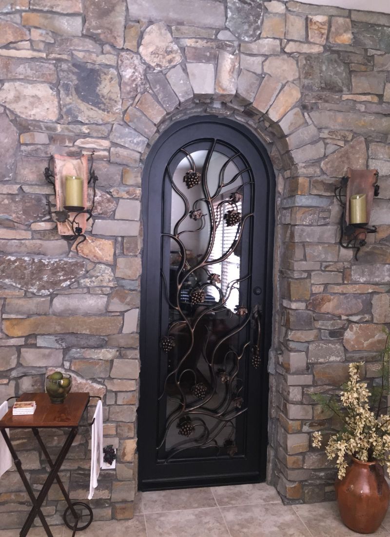 Elegant arched door with decorative metalwork on a stone wall, accented by candle sconces and natural decor.